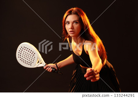 Woman preparing to play paddle tennis in a dramatic lighting setup indoors 133244291