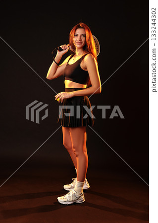 Woman posing confidently with a racket in a stylish tennis outfit indoors 133244302