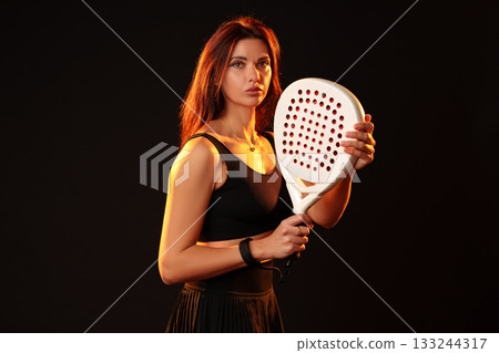 Female athlete poses confidently with a racket in a dramatic lighting setup Female athlete poses confidently with a racket in a dramatic lighting setup 133244317