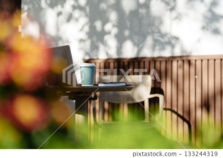 Cozy outdoor workspace with laptop, coffee, and vibrant flowers in a tranquil setting 133244319