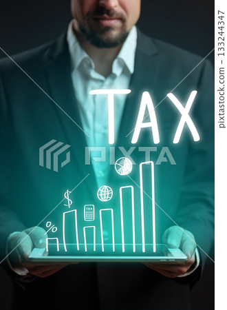 Businessman holding tablet displaying tax-related graphs and symbols in dark room Businessman holding tablet displaying tax-related graphs and symbols in dark room 133244347