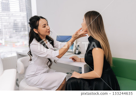 Asian female doctor in white robe consulting woman patient in office, discussing medical matters, providing healthcare information during professional visit. Concept of healthy lifestyle. 133244635