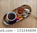 A cup of coffee and a cup of tea served on a golden tray with a spoon on a wooden table.  133244894