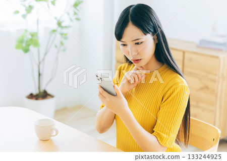 一位年輕女子一邊擔憂地看著她的智慧型手機一邊煩惱。 一位年輕女子一邊擔憂地看著她的智慧型手機一邊煩惱。 133244925