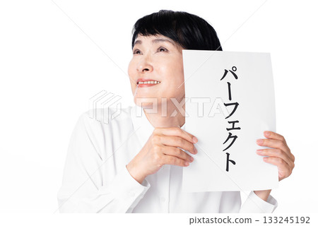 A senior woman wearing a white shirt smiling happily and holding a piece of paper with the word "Perfect" written on it in both hands A senior woman wearing a white shirt smiling happily and holding a piece of paper with the word "Perfect" written on it in both hands 133245192