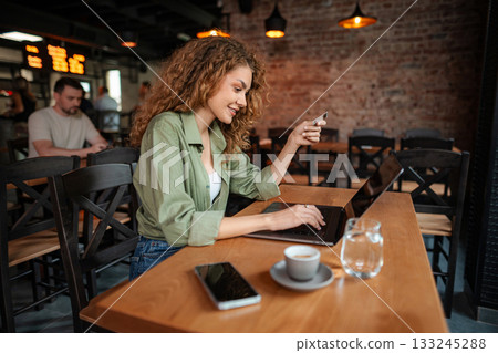 Young Woman Making Online Payment with Credit Card in Cafe 133245288