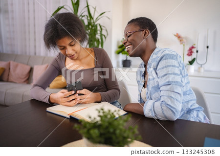 Two young black women laughing while looking at smartphone at home Two young black women laughing while looking at smartphone at home 133245308