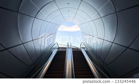The upward-moving escalator is framed by a sleek, curved ceiling, creating a sense of depth and leading the eye upwards 133245446