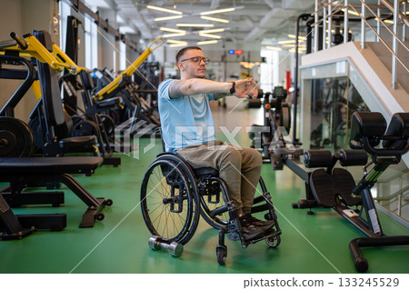 Male athlete in wheelchair stretching arms, doing warm up for upper body power exercises at gym. Male athlete in wheelchair stretching arms, doing warm up for upper body power exercises at gym. 133245529