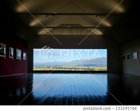 The gallery's polished wooden floor reflects the stunning view of mountains and a vibrant sky, creating a unique perspective 133245788