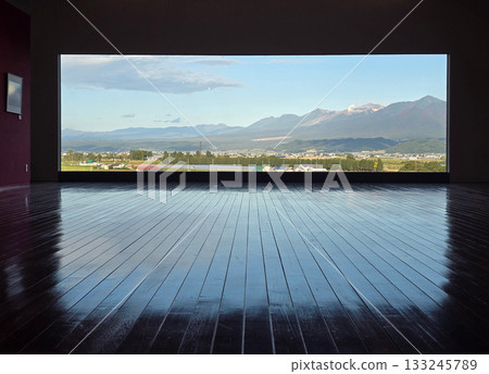 The gallery's polished wooden floor reflects the stunning view of mountains and a vibrant sky, creating a unique perspective 133245789