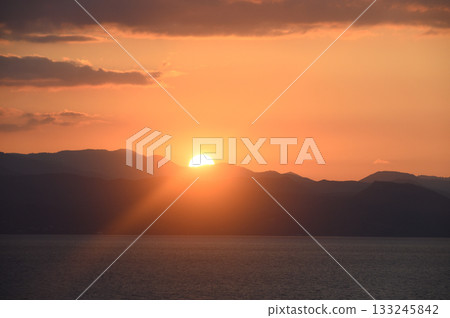 Golden sunset casts a warm glow over tranquil mountains and serene waters in a picturesque landscape 133245842