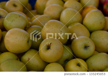 Golden apples piled high at a vibrant market during a sunny afternoon harvest festival 133245853