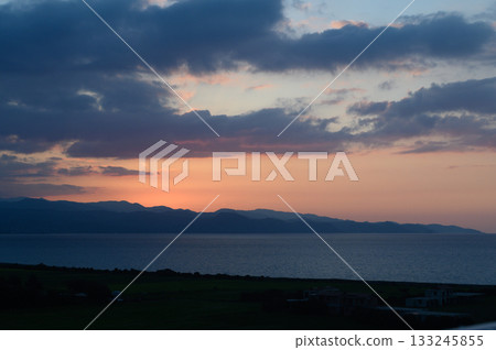 Golden hues embrace the horizon as twilight softly descends over distant mountains 133245855