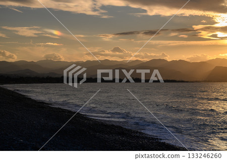 Sunset over tranquil waters with distant mountains and colorful clouds dancing in the evening sky 133246260