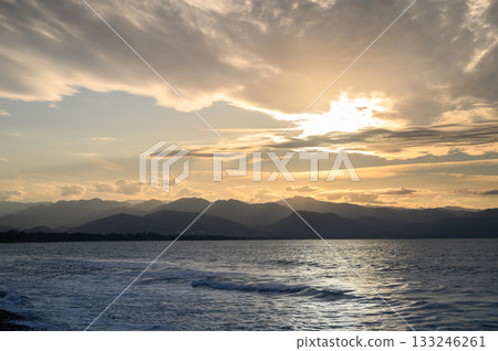 Golden sunset over tranquil waters with distant mountains creating a serene landscape in the evening sky Golden sunset over tranquil waters with distant mountains creating a serene landscape in the evening sky 133246261