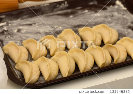 Dumplings arranged neatly on a tray ready for steaming in a cozy kitchen setting Dumplings arranged neatly on a tray ready for steaming in a cozy kitchen setting 133246285