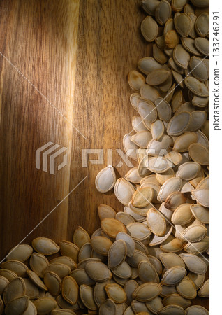 Brightly lit pumpkin seeds scattered on a wooden surface drying in the warm afternoon sun Brightly lit pumpkin seeds scattered on a wooden surface drying in the warm afternoon sun 133246291