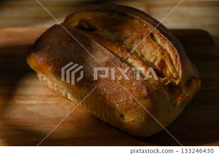 Freshly baked bread resting on a wooden board waiting to be sliced in a cozy kitchen 133246430