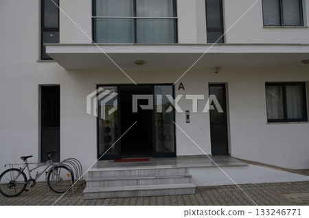 Entrance of a modern building with bicycle parked nearby on a quiet street during overcast weather Entrance of a modern building with bicycle parked nearby on a quiet street during overcast weather 133246771