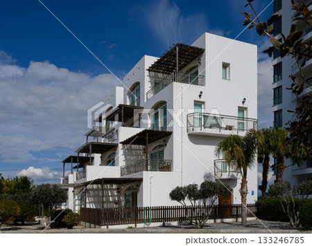 Modern white building surrounded by lush greenery under a bright blue sky in a peaceful neighborhood Modern white building surrounded by lush greenery under a bright blue sky in a peaceful neighborhood 133246785