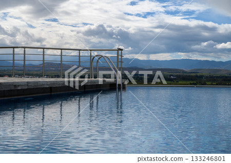 Serene infinity pool overlooking lush valleys and majestic mountains under a cloudy sky Serene infinity pool overlooking lush valleys and majestic mountains under a cloudy sky 133246801