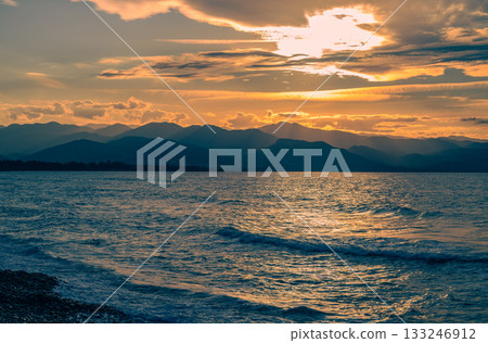 Sunset over tranquil waters with mountains in the distance creates a serene atmosphere 133246912