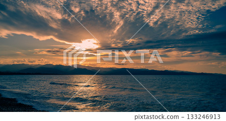 Sunset hues dance across the water with distant mountains framing the horizon 133246913