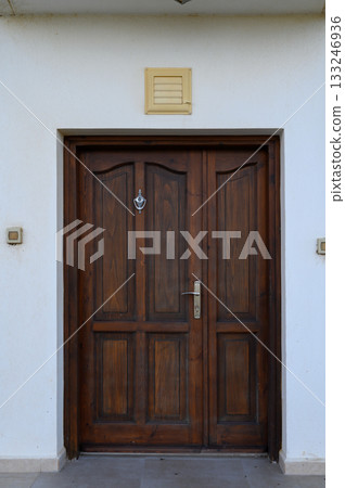 Beautiful wooden door adorned with a decorative knocker against a minimalist exterior design 133246936