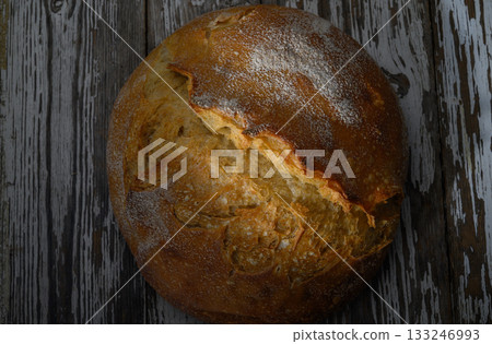 Freshly baked rustic bread with a crispy crust resting on a wooden table 133246993