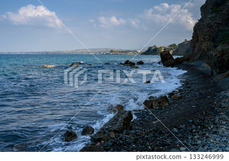 Waves gently lapping against rocky shoreline at dusk near a serene coastal village Waves gently lapping against rocky shoreline at dusk near a serene coastal village 133246999