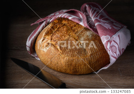 Freshly baked round bread wrapped in a cozy cloth on a wooden surface 133247085