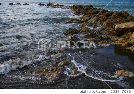 Waves gently lap against rocky shore at sunset with vibrant colors atmosphere Waves gently lap against rocky shore at sunset with vibrant colors atmosphere 133247086