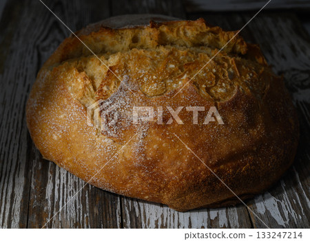 Freshly baked artisan bread resting on rustic wooden surface in warm golden light 133247214