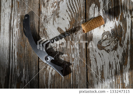 Corkscrew and cork resting on rustic wooden table in warm sunlight, a moment before the gathering begins 133247315