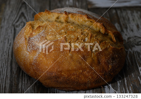 Freshly baked artisan bread resting on rustic wooden table under warm light Freshly baked artisan bread resting on rustic wooden table under warm light 133247328