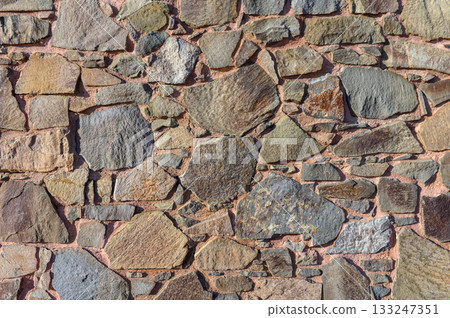 Natural stone wall displays an array of textures and colors under sunlight in a serene setting Natural stone wall displays an array of textures and colors under sunlight in a serene setting 133247351