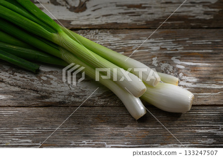 Fresh green onions arranged on a rustic wooden surface highlighting their vibrant colors and textures Fresh green onions arranged on a rustic wooden surface highlighting their vibrant colors and textures 133247507