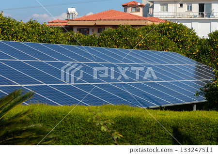 Solar panels shine brightly under the clear sky in a lush garden surrounded by modern architecture 133247511
