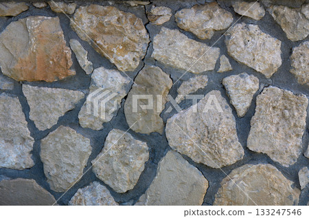 Textured stone wall showcasing natural patterns and earthy tones in sunlight 133247546