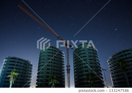 Nighttime skyline shows construction cranes against a starry sky in a modern urban setting Nighttime skyline shows construction cranes against a starry sky in a modern urban setting 133247586