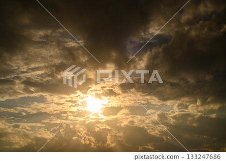 Golden rays pierce through dramatic clouds during a tranquil sunset sky 133247686