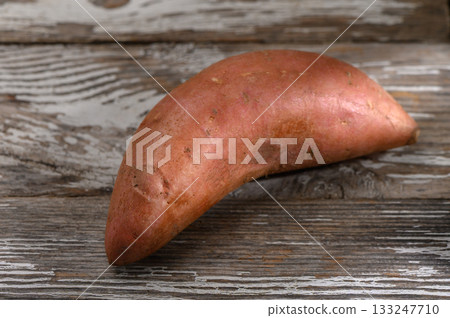 Sweet potato resting on rustic wooden surface highlighting its unique shape and vibrant color Sweet potato resting on rustic wooden surface highlighting its unique shape and vibrant color 133247710