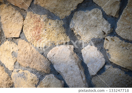Rustic stone wall showcases natural textures and earthy tones in warm sunlight Rustic stone wall showcases natural textures and earthy tones in warm sunlight 133247718