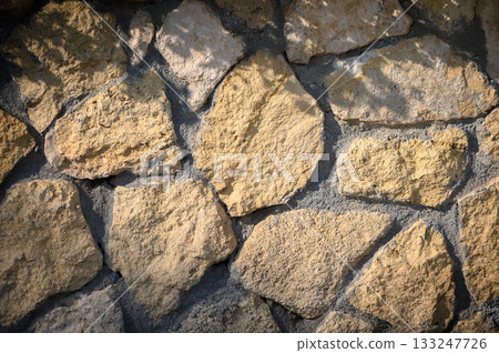 Natural sunlight casts gentle shadows on a rustic stone wall in a serene outdoor setting 133247726