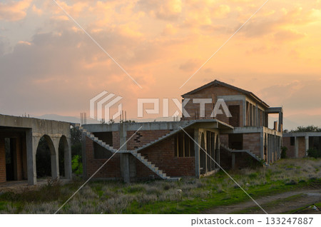 Sunset illuminates an abandoned building under a vibrant sky in a quiet landscape 133247887