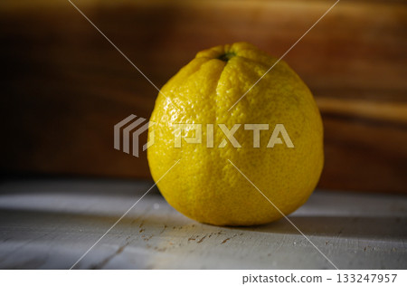 Vibrant yellow lemon resting on a rustic wooden surface under natural light 133247957