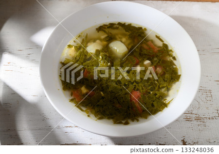 Delicious green soup garnished with fresh herbs and vegetables served in bright daylight Delicious green soup garnished with fresh herbs and vegetables served in bright daylight 133248036