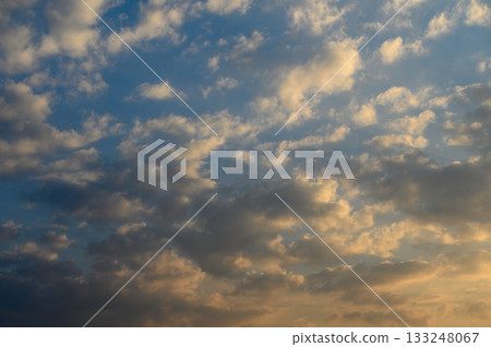 Soft clouds dance across a vibrant sky at dusk over a tranquil landscape Soft clouds dance across a vibrant sky at dusk over a tranquil landscape 133248067