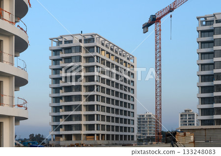 Urban development project with modern buildings rising under construction crane at twilight 133248083